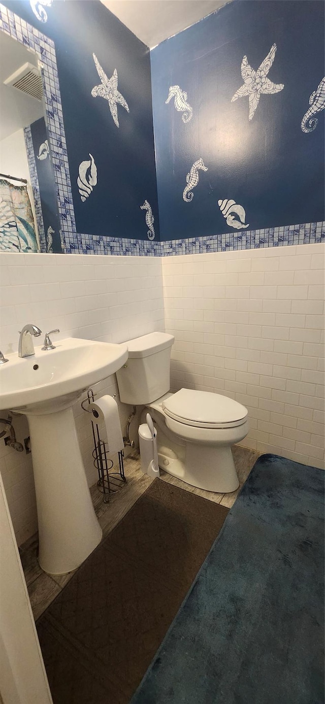 bathroom featuring toilet, tile walls, visible vents, and a wainscoted wall