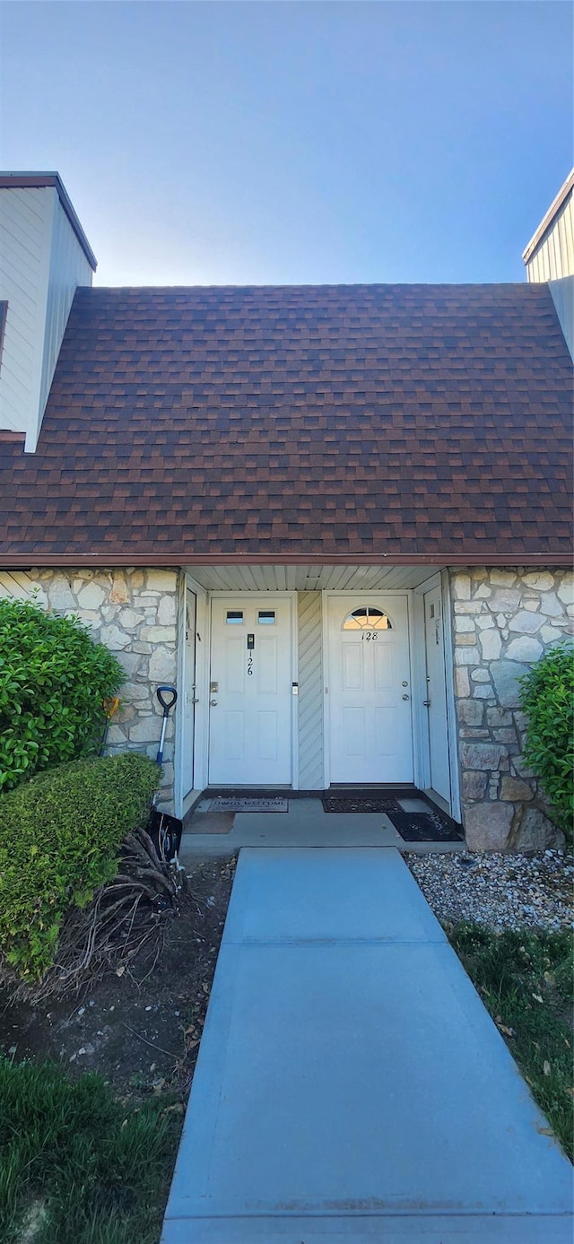 entrance to property with roof with shingles and stone siding