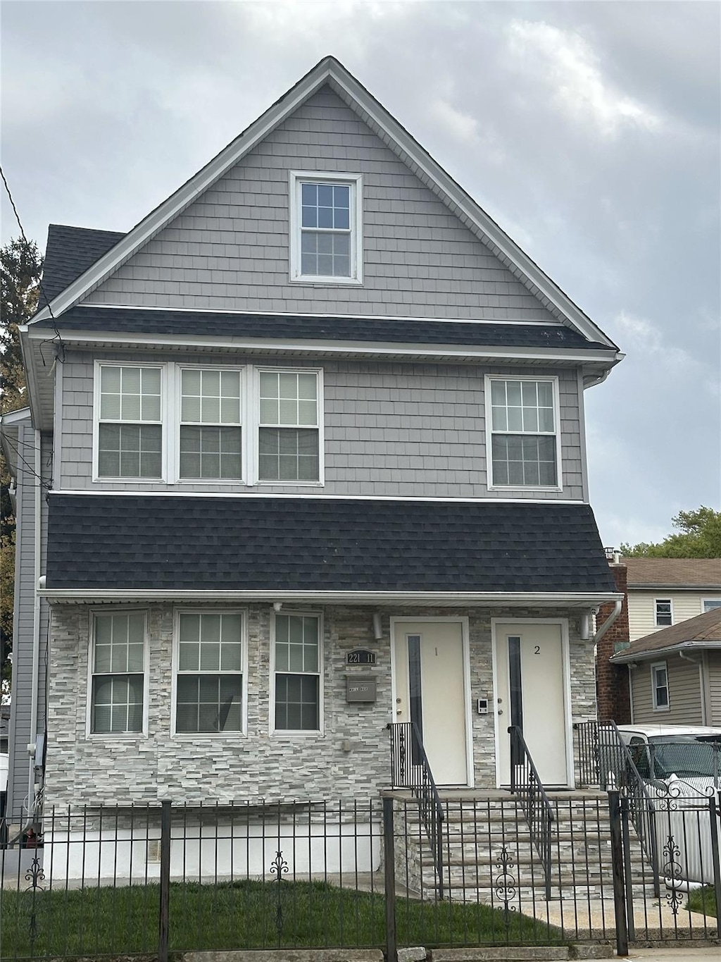view of front facade featuring a shingled roof, a fenced front yard, and stone siding