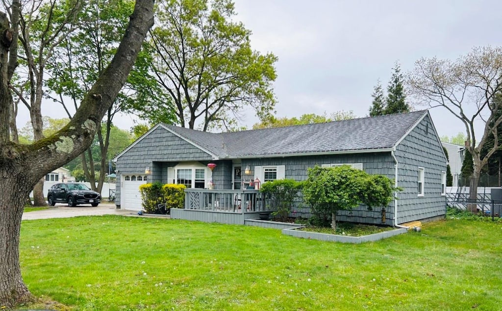 ranch-style house with roof with shingles, an attached garage, concrete driveway, and a front lawn