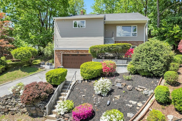 view of front facade featuring brick siding, an attached garage, driveway, and a chimney