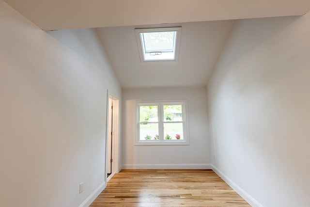 empty room featuring light wood finished floors, vaulted ceiling, and baseboards