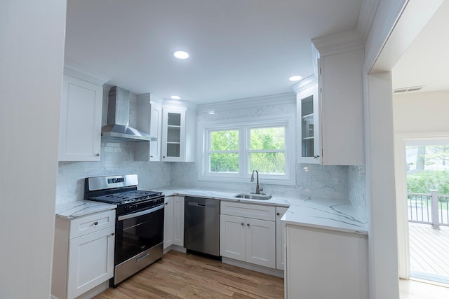 kitchen with wall chimney range hood, stainless steel appliances, a healthy amount of sunlight, and a sink