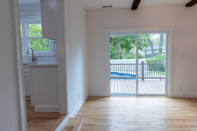 doorway with light wood-type flooring, visible vents, baseboards, and a sink