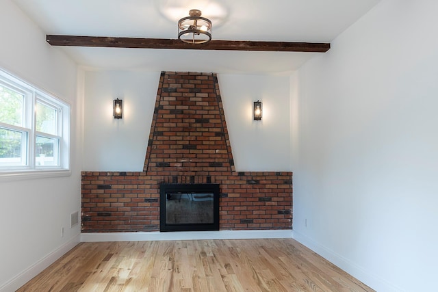 unfurnished living room with a fireplace, beamed ceiling, visible vents, and wood finished floors
