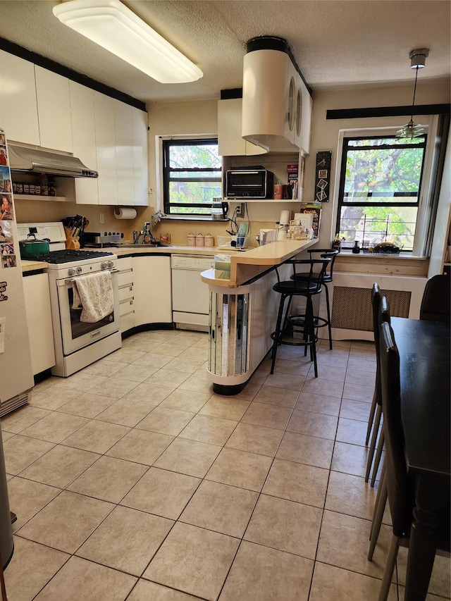 kitchen featuring a textured ceiling, white cabinetry, under cabinet range hood, and white appliances