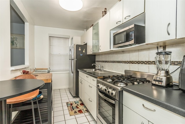 kitchen with a sink, tasteful backsplash, glass insert cabinets, light tile patterned floors, and appliances with stainless steel finishes