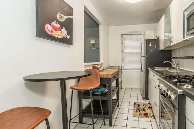 kitchen featuring light tile patterned floors, a sink, white cabinetry, backsplash, and stainless steel appliances