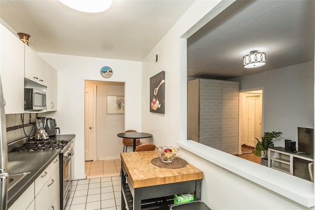kitchen featuring light tile patterned floors, wood counters, stainless steel appliances, white cabinets, and decorative backsplash