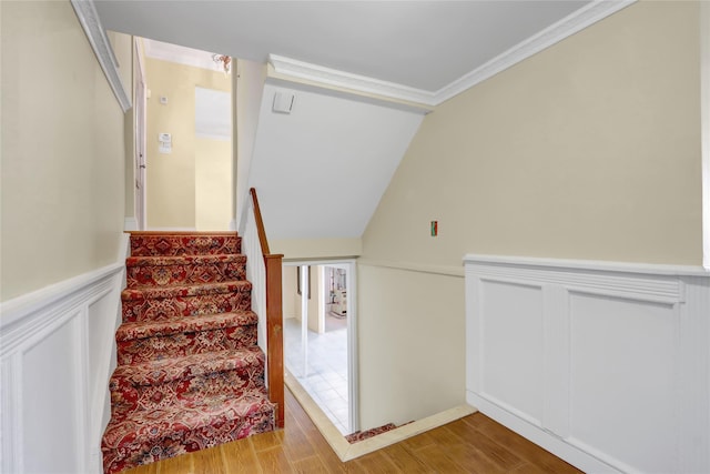 staircase featuring a decorative wall, crown molding, wood finished floors, and wainscoting