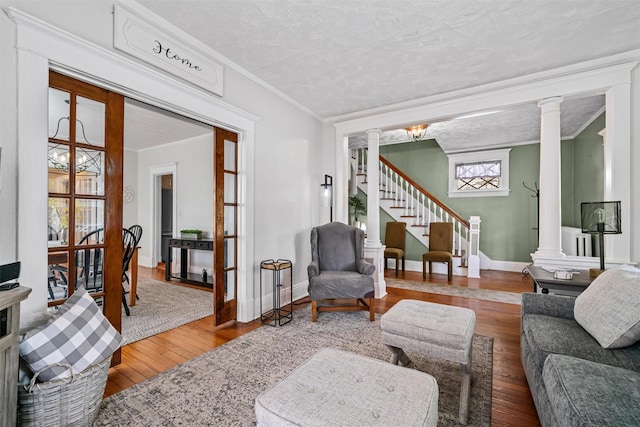 living area featuring crown molding, hardwood / wood-style flooring, stairway, and ornate columns