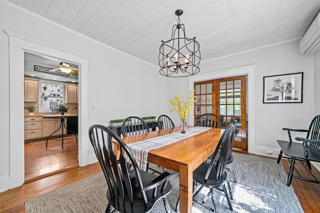 dining area featuring french doors, a wall mounted air conditioner, wood-type flooring, an inviting chandelier, and ornamental molding