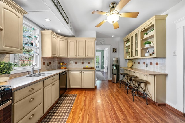 kitchen with decorative backsplash, black dishwasher, a sink, light wood finished floors, and range