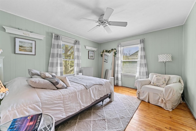 bedroom with wood-type flooring, a ceiling fan, radiator, and multiple windows
