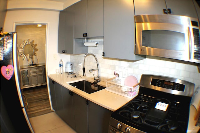 kitchen featuring a sink, stainless steel appliances, tasteful backsplash, gray cabinets, and light countertops