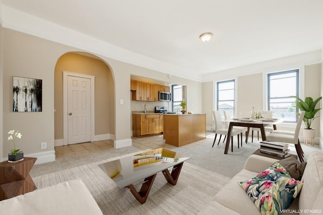 living area with arched walkways, baseboards, and light colored carpet