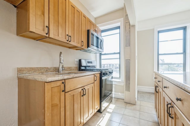kitchen with light stone countertops, baseboards, a sink, light tile patterned floors, and stainless steel appliances