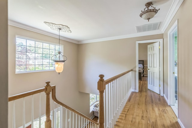 hallway with visible vents, baseboards, an upstairs landing, light wood-style floors, and ornamental molding