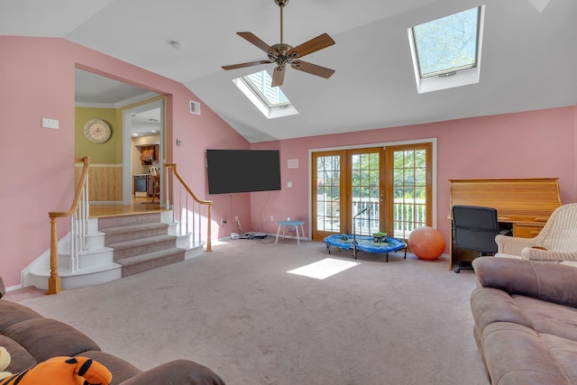 carpeted living area with visible vents, a ceiling fan, vaulted ceiling with skylight, and stairway