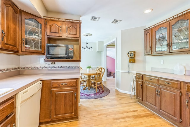 kitchen featuring black microwave, dishwasher, light countertops, brown cabinetry, and visible vents