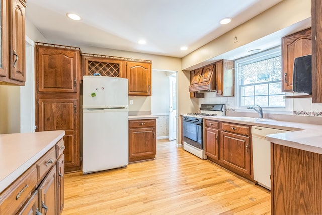 kitchen featuring brown cabinets, a sink, light countertops, light wood finished floors, and white appliances