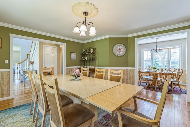 dining room with an inviting chandelier, crown molding, stairs, and hardwood / wood-style floors