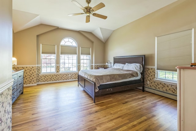 bedroom with a ceiling fan, baseboard heating, vaulted ceiling, light wood-style floors, and wallpapered walls