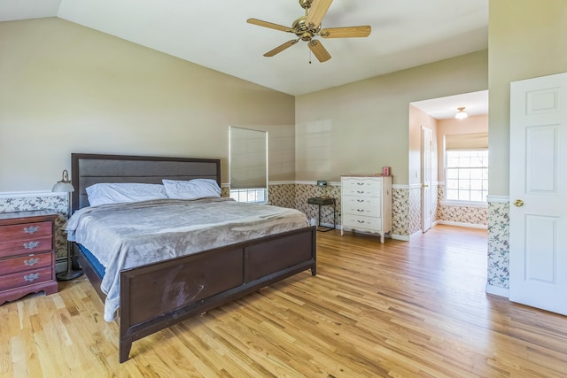 bedroom with light wood-style flooring, ceiling fan, a wainscoted wall, and vaulted ceiling