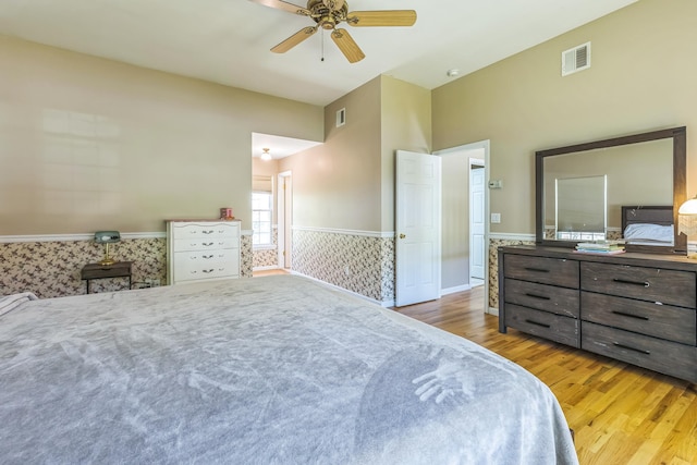 bedroom featuring ceiling fan, visible vents, wainscoting, and wood finished floors