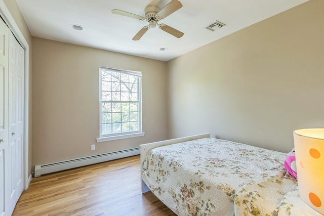 bedroom featuring ceiling fan, visible vents, wood finished floors, a baseboard radiator, and a closet