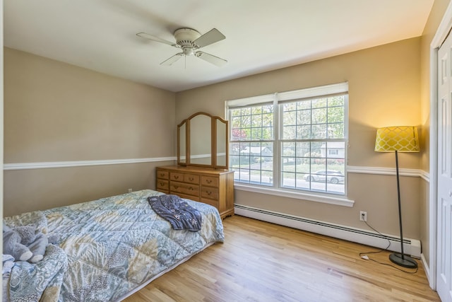 bedroom with a ceiling fan, a baseboard heating unit, and wood finished floors