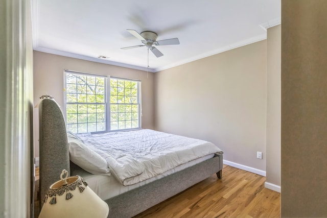 bedroom with a ceiling fan, baseboards, light wood-type flooring, visible vents, and ornamental molding