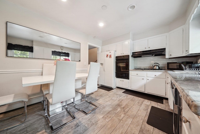 kitchen with black appliances, under cabinet range hood, a warming drawer, backsplash, and light wood-style flooring