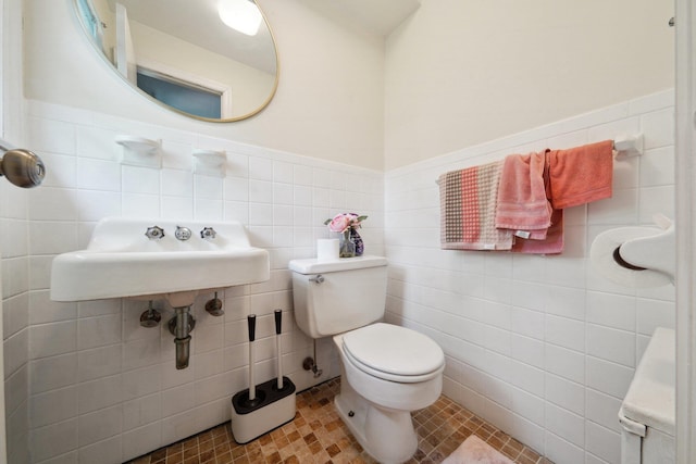 bathroom with tile walls, toilet, wainscoting, and a sink