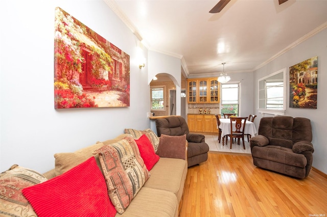 living room featuring light wood-style floors, arched walkways, ceiling fan, and crown molding