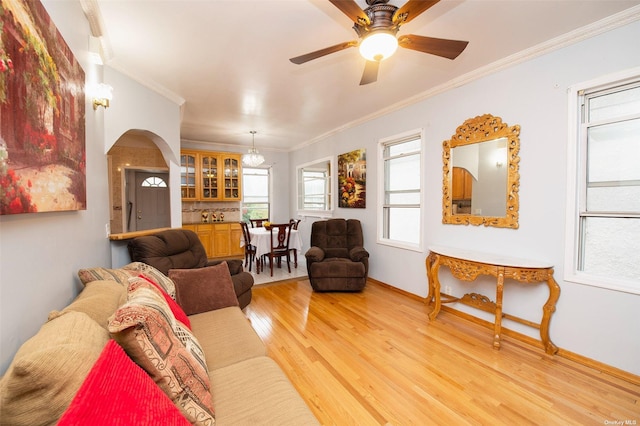 living area with crown molding, baseboards, ceiling fan, arched walkways, and light wood-style flooring