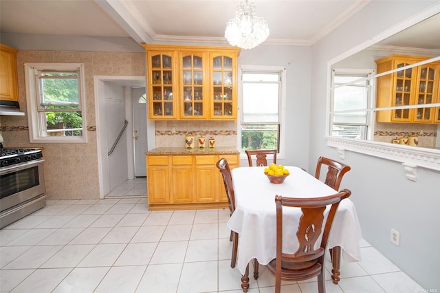 kitchen with glass insert cabinets, stainless steel gas range oven, an inviting chandelier, ornamental molding, and under cabinet range hood