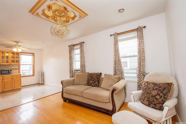 living room featuring baseboards, a ceiling fan, light wood-style floors, and radiator heating unit