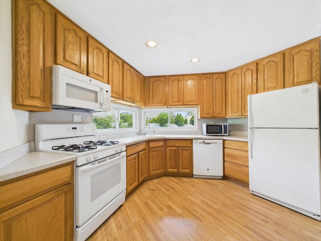 kitchen featuring white appliances, a sink, brown cabinetry, light countertops, and light wood-type flooring