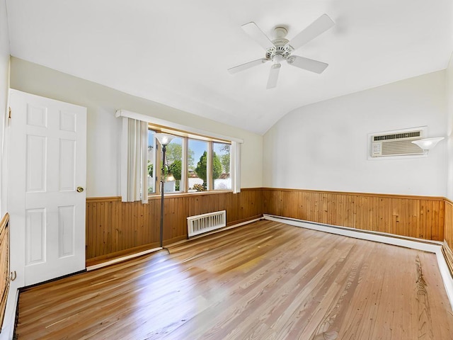 unfurnished room featuring a wainscoted wall, radiator heating unit, wood walls, wood finished floors, and lofted ceiling