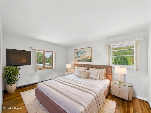 bedroom featuring multiple windows, wood finished floors, and a baseboard heating unit