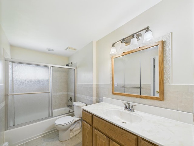 bathroom featuring toilet, tile walls, vanity, bath / shower combo with glass door, and tile patterned flooring