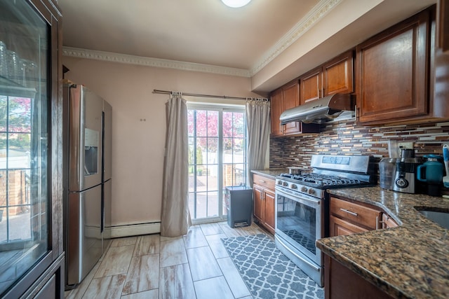kitchen featuring dark stone countertops, baseboard heating, under cabinet range hood, appliances with stainless steel finishes, and decorative backsplash