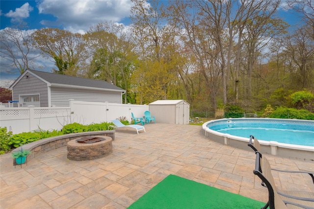 view of pool with an outbuilding, a shed, an outdoor fire pit, a patio area, and a fenced backyard