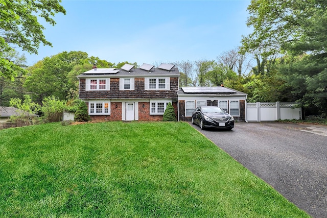 view of front of home with fence, driveway, a front lawn, solar panels, and a chimney
