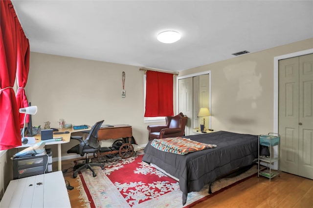 bedroom featuring multiple closets, visible vents, and wood finished floors