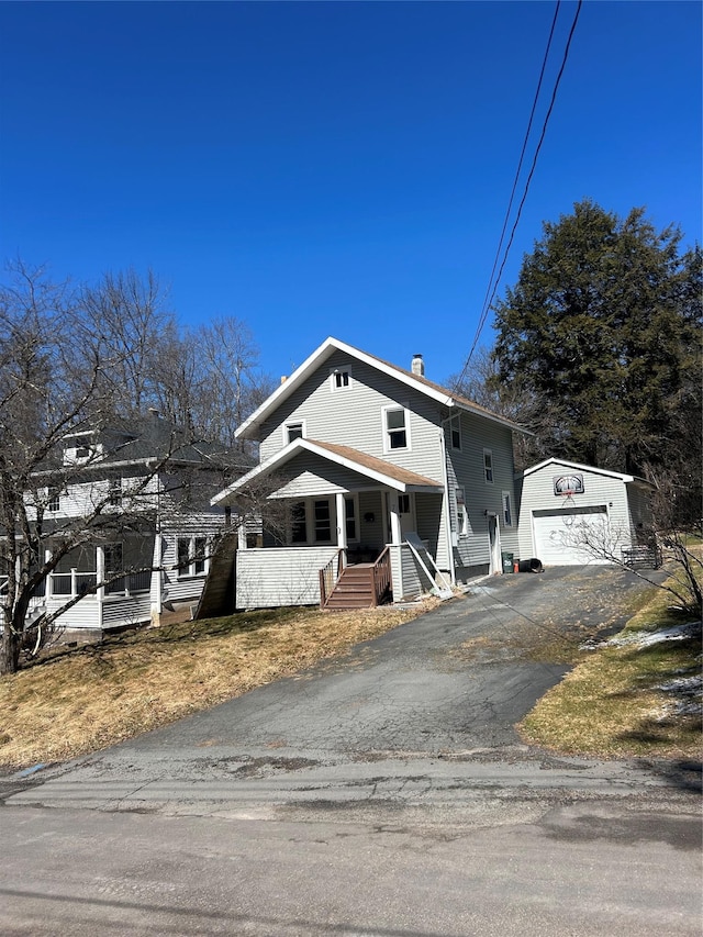 view of front of house with covered porch, a chimney, an outbuilding, driveway, and a detached garage