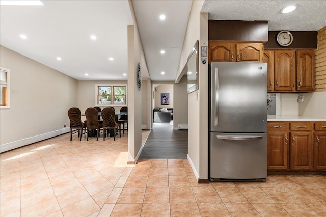 kitchen with freestanding refrigerator, brown cabinetry, light countertops, recessed lighting, and baseboards