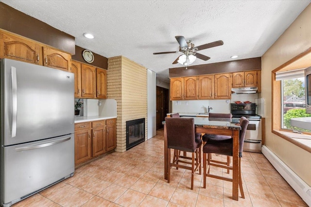 kitchen with appliances with stainless steel finishes, a baseboard radiator, under cabinet range hood, ceiling fan, and brown cabinets