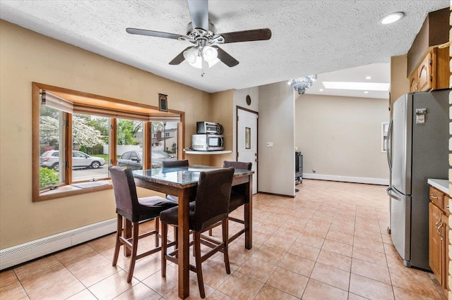 dining room featuring ceiling fan, a baseboard heating unit, a textured ceiling, light tile patterned flooring, and baseboards